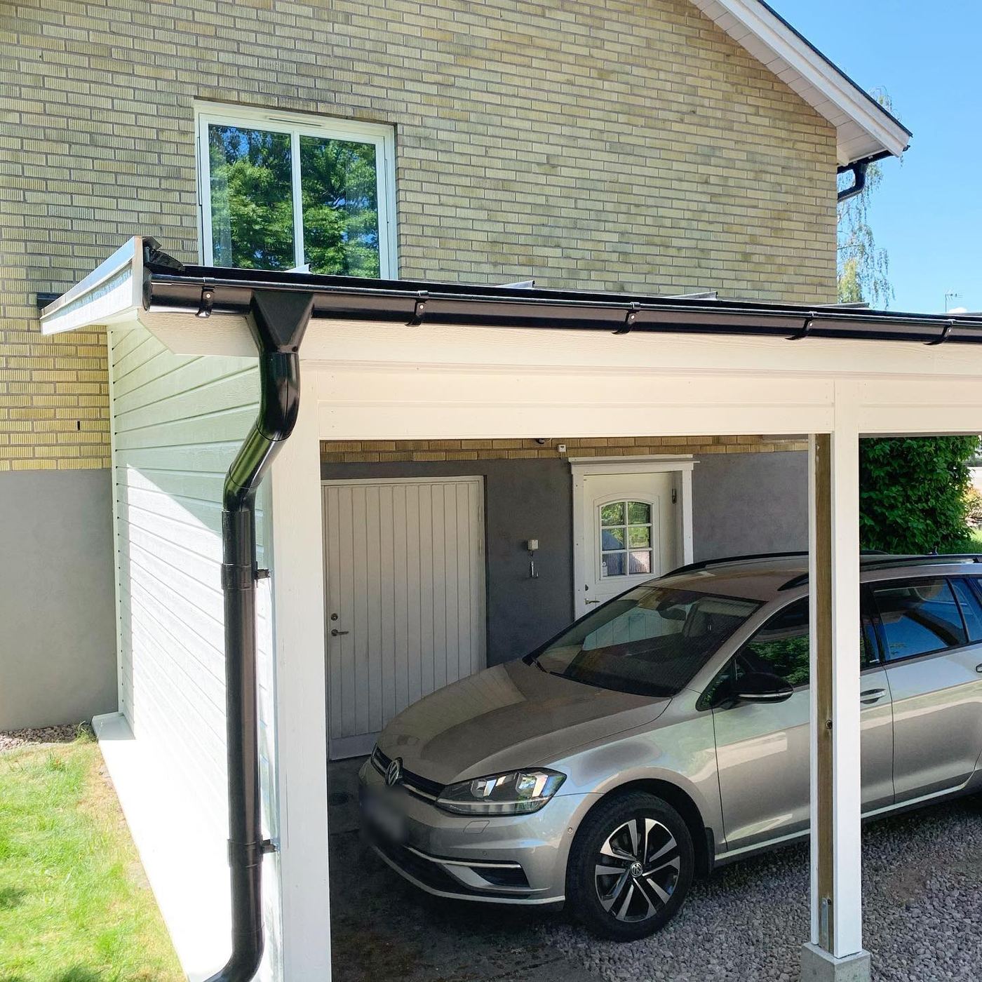 Vit carport med svarta hängrännor vid ett tegelhus