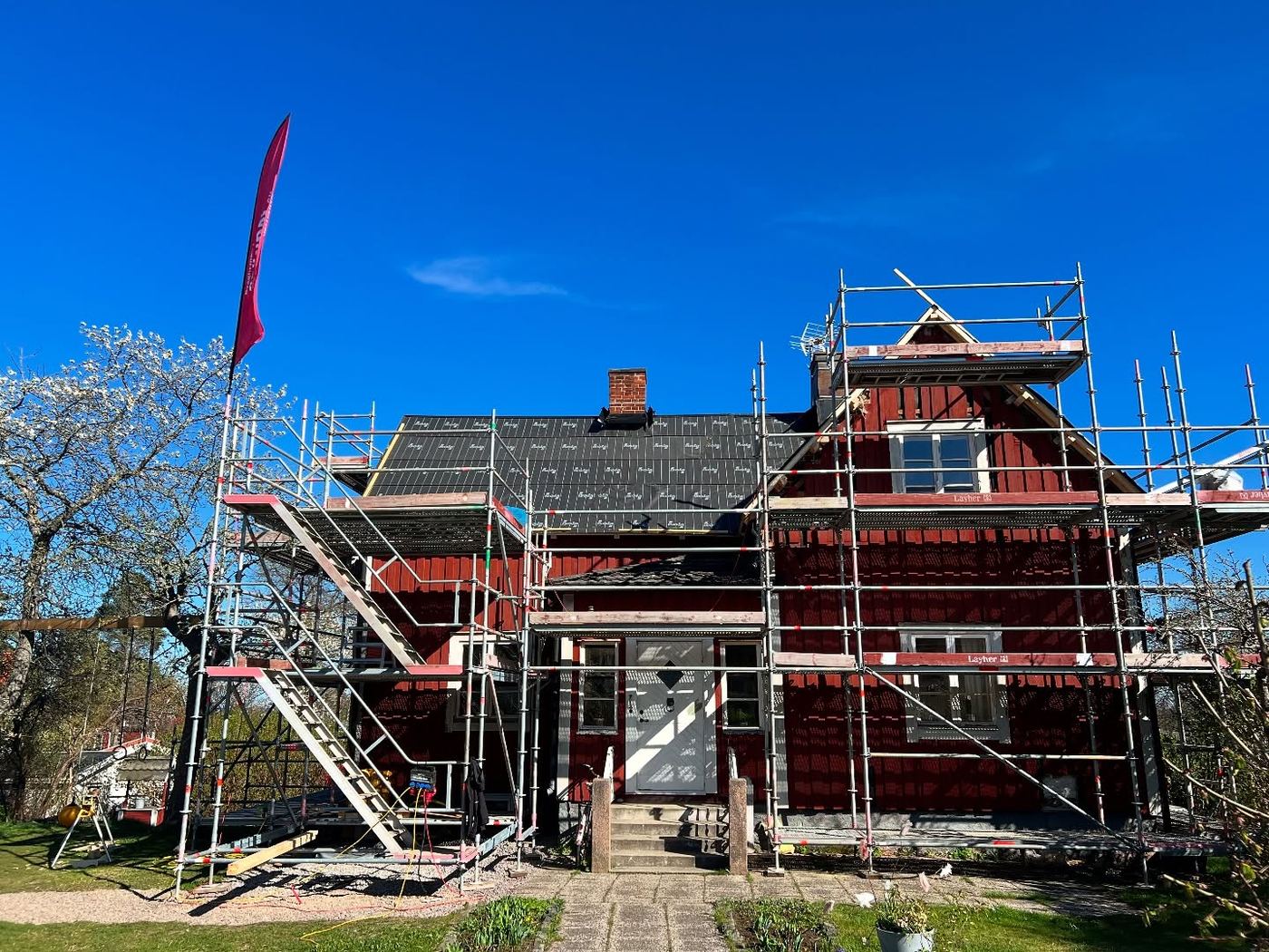 Rött trähus i byggnadsställning som får ny fasad, nytt tak, nya fönster och en tillbyggnad