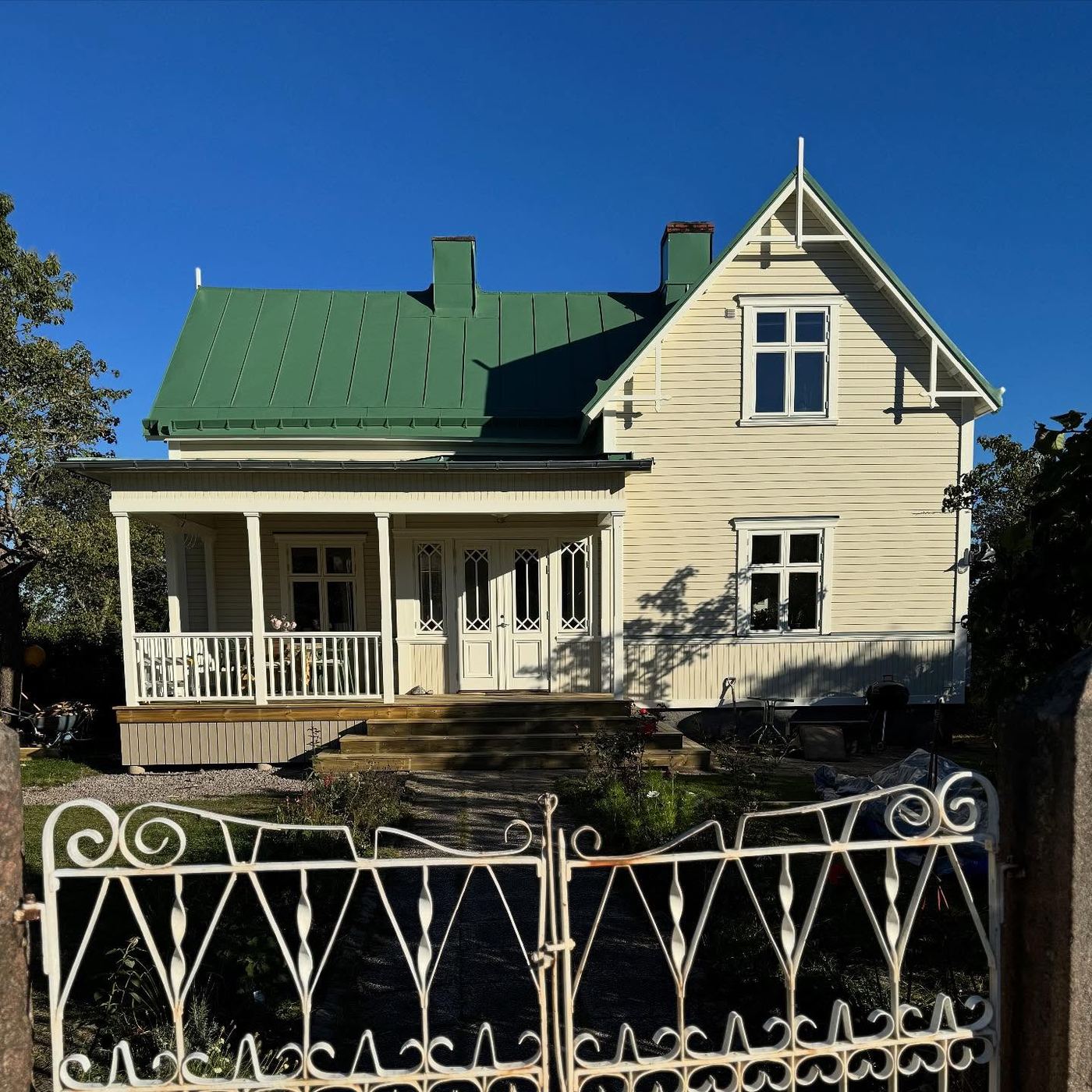 Renoverat sekelskifteshus i ljusgult med grönt plåttak och veranda