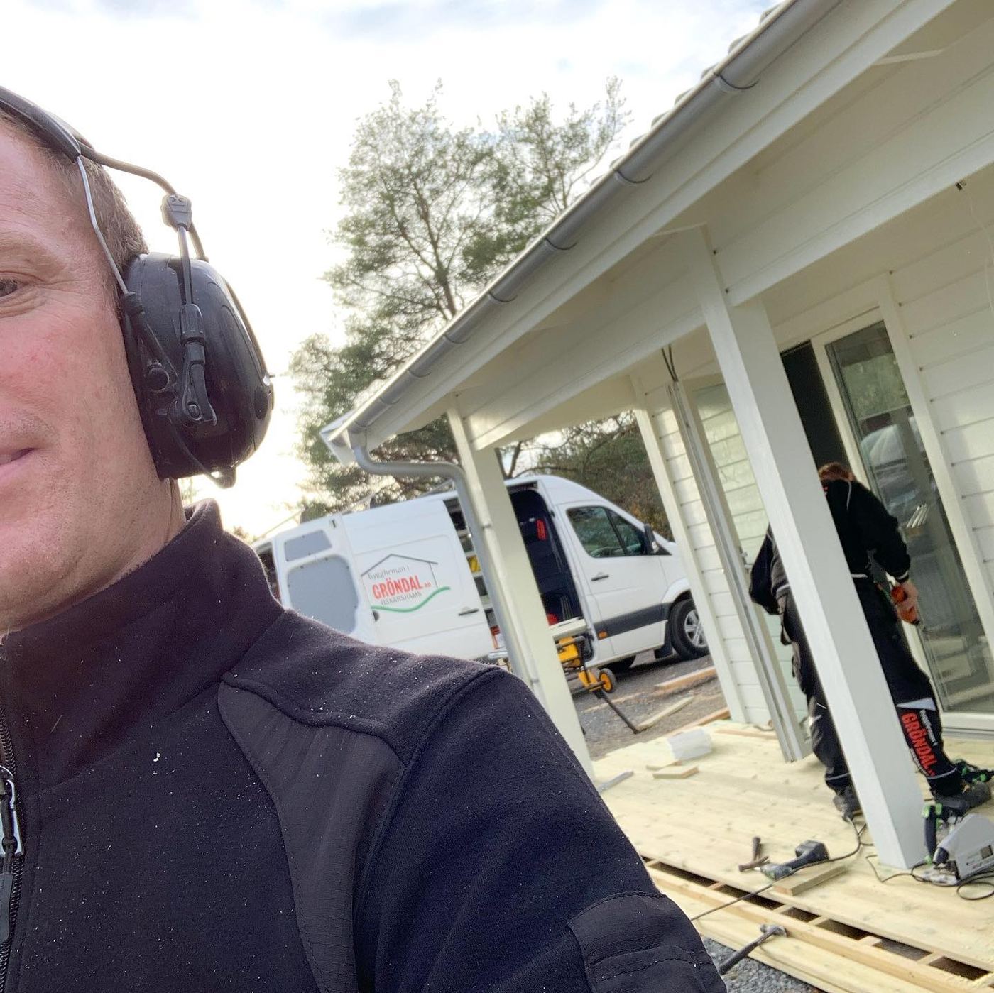 Snickare från Gröndals Bygg med hörselskydd vid ett altanbygge, firmabilen i bakgrunden
