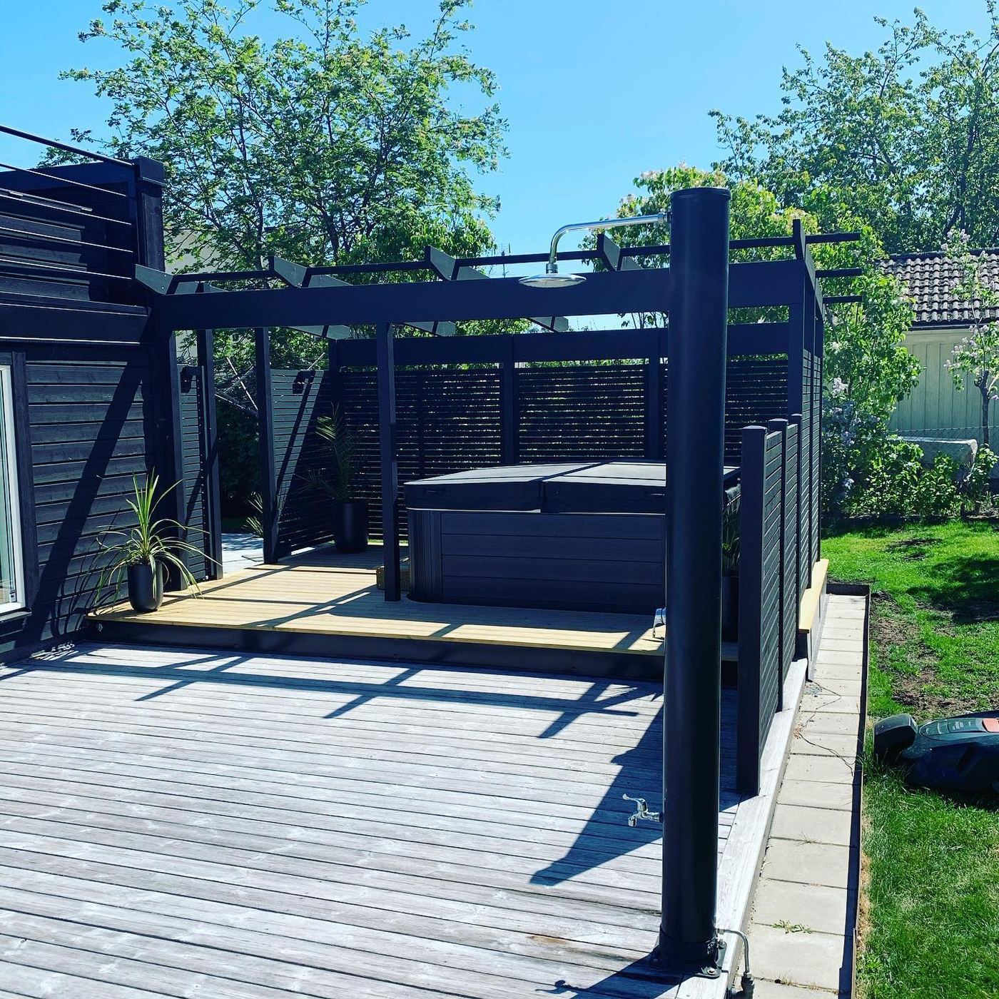 Spabad med svart pergola, insynsskydd och utedusch på trädäck